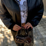 Load image into Gallery viewer, Person in black leather jacket and leopard print pants holding a Y2K BROWN BELTED handbag.
